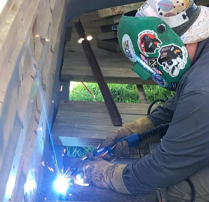 photo of a man in a welding hood repairing a weld on a trailer